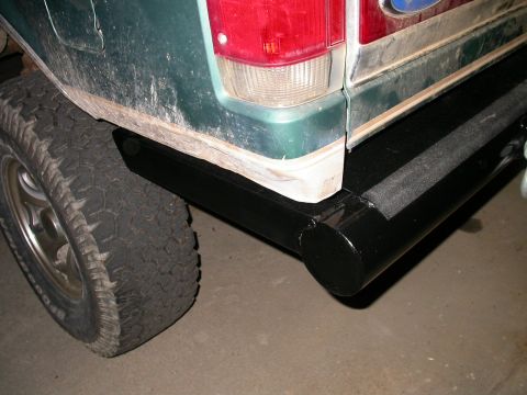 1990 Ford Bronco - Close-up of the passenger-side rear corner of a green Ford SUV showing a black capped tube bumper with a welded end cap tucked under the de…