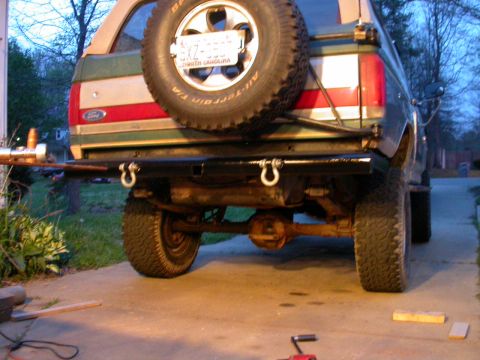 1990 Ford Bronco - Rear view of a green and tan two-tone Ford SUV at dusk with a fresh black tube bumper mock-up clamped in place, chrome D-ring shackles hang…