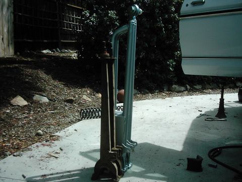 1978 Ford Bronco - Two suspension radius arms stood upright on a concrete driveway for comparison, a rusty original cast arm beside a freshly zinc-plated tubu…