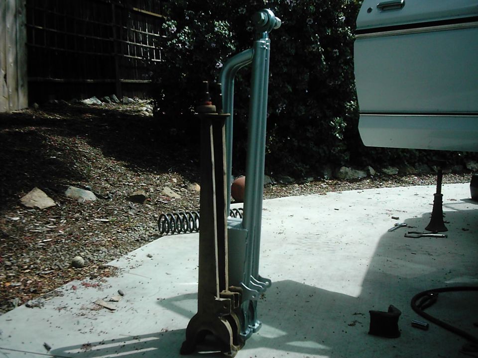 Rusty stock radius arm next to a new zinc-plated tubular arm on a driveway