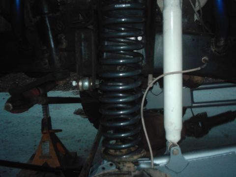 1978 Ford Bronco - Close-up under a lifted 4x4 showing a tall dark coil spring seated on the axle-side spring perch, with a white-bodied shock absorber runnin…