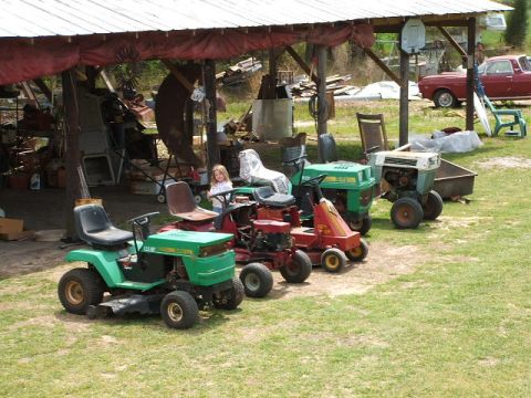 1966 Ford Ranchero - A collection of lawnmowers are visible under a rustic shelter, with a young girl seated on one of the machines.