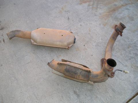 1993 Ford Bronco - Two rusty exhaust system components are laid out on a concrete surface, one appearing to be a catalytic converter and the other a bent pipe.