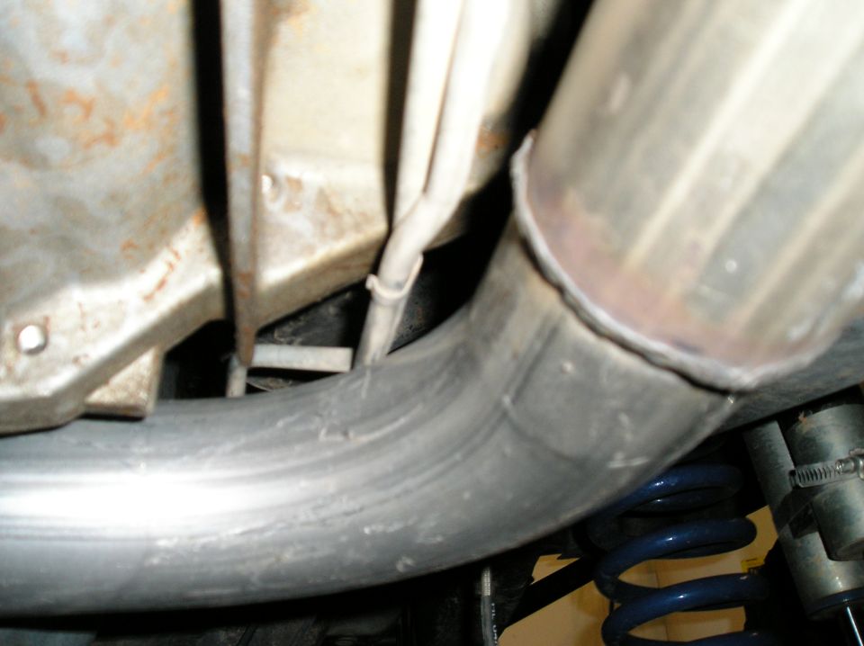 Underbody exhaust pipe with welded joint near blue coil spring