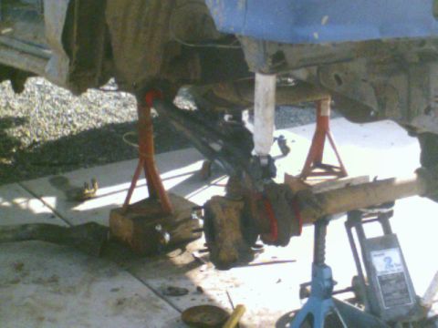 1989 Ford Bronco - Undercarriage of a vehicle undergoing suspension work, supported by jack stands and a hydraulic jack.