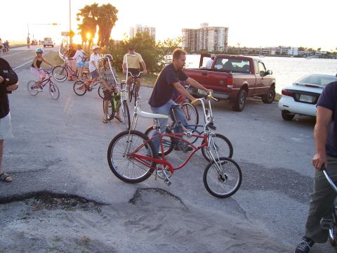 1994 Ford Probe - A group of people ride bicycles on a street near a body of water.