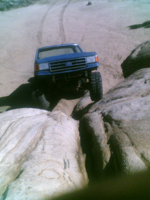 1989 Ford Bronco - This blue Ford F-Series truck is shown off-roading over large rocks.