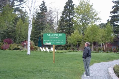 1989 Ford Bronco - A sign in a grassy area reads 'Welcome to Ontario' with a provocative statement below it.