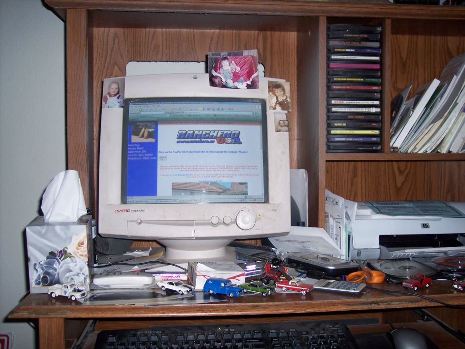 Computer monitor showing a website with 'RANCHERO USA' logo. Desk has toy cars and a printer