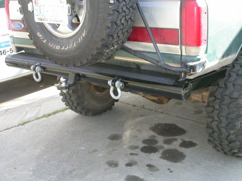 1990 Ford Bronco - Rear view of a green Ford Bronco showing a custom black tubular steel rear bumper with two D-ring shackles and a receiver hitch. The truck…