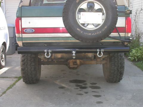 1990 Ford Bronco - Straight-on rear view of a green and tan two-tone Ford Bronco on a concrete driveway, fitted with a heavy black tubular rear bumper carryin…