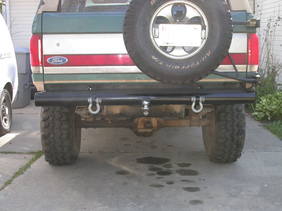 Rear view of a green and tan Ford Bronco with black tube bumper, D-ring shackles and swing-out spare