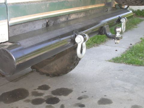 1990 Ford Bronco - Low-angle view of a shop-built black tube rear bumper welded to a green SUV, fitted with two chrome D-ring shackles and a receiver hitch wi…