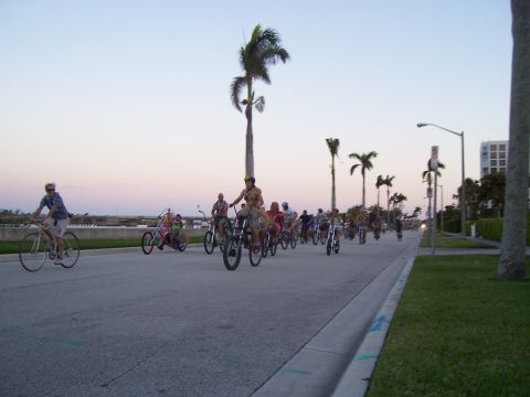 1994 Ford Probe - A group of cyclists ride down a street lined with palm trees as the sun sets.