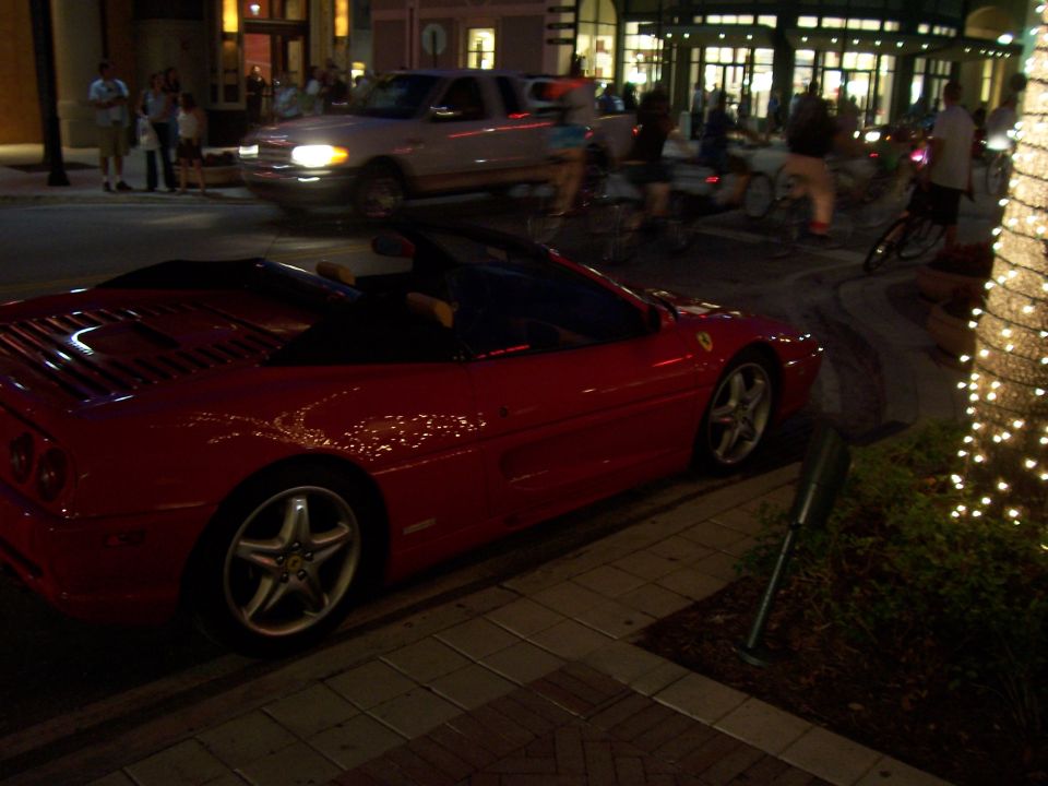 Red Ferrari convertible parked top-down at a downtown curb at night