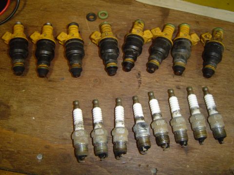 1989 Ford Bronco - A collection of automotive parts, including fuel injectors and spark plugs, are laid out on a wooden table.