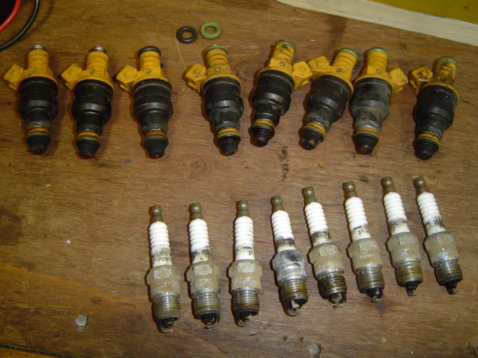 Eight removed fuel injectors and eight used spark plugs on a workbench