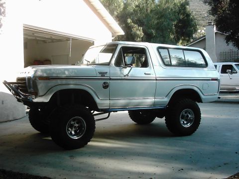 1978 Ford Bronco - White lifted full-size Ford Bronco with its hardtop installed, photographed in side profile on a driveway in front of an open garage. It ha…