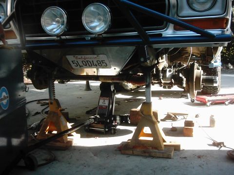 1978 Ford Bronco - Low front-end shot of a white Ford 4x4 raised on yellow jack stands and a 3-ton Craftsman floor jack, with the right front wheel removed to…