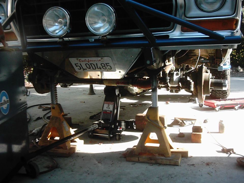 White Ford 4x4 on jack stands in driveway with front wheel off exposing brake rotor
