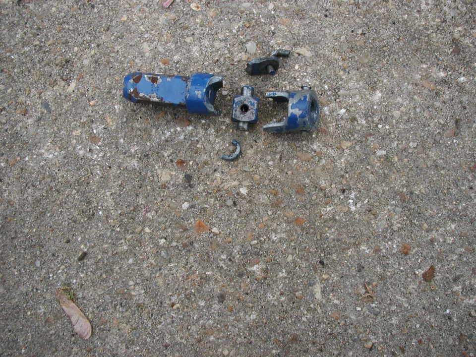 Broken blue-painted U-joint and yoke parts scattered on concrete pavement