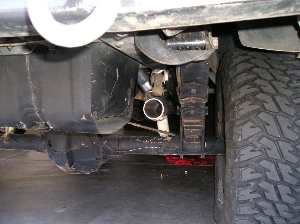 Undercarriage of lifted 4x4 showing axle, leaf springs, driveshaft and cut exhaust pipe