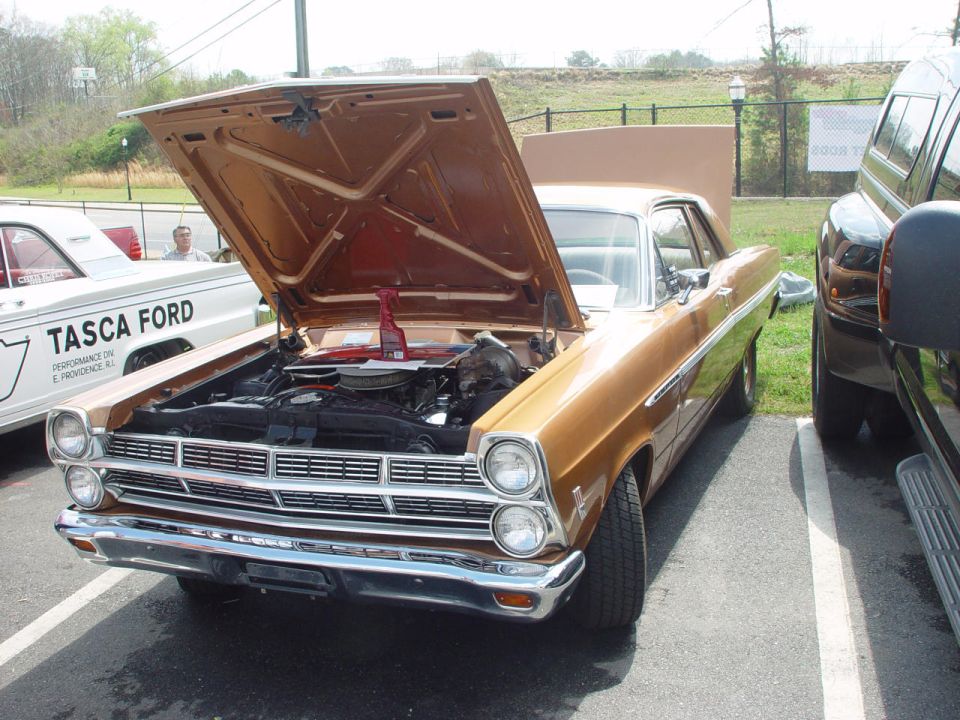 Gold Ford Fairlane hardtop at a car show with hood open showing its V8 engine