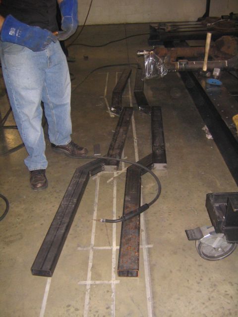 1978 Ford Bronco - A person in jeans and welding gloves works on metal components laid out on a grid pattern on the floor.