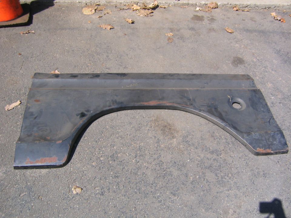 Dark metal rear fender panel with wheel arch cutout, lying on asphalt