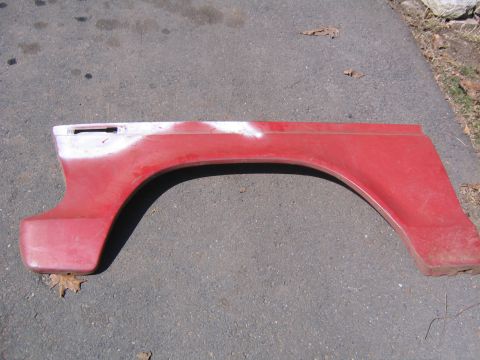1978 Ford Bronco - A red fender part, possibly for a truck or SUV, lies on asphalt.