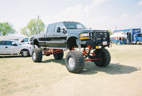 1989 Ford F-350 - Modified black Ford pickup truck with extensive lift kit and oversized tires on display.