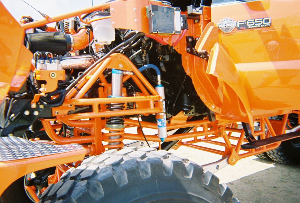 Orange Ford F-650 Super Duty front suspension with large tire and custom roll cage