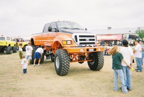 1989 Ford F-350 - This heavily modified orange Ford truck features oversized tires and a lifted suspension, seen at an outdoor event.