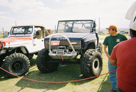 1989 Ford F-350 - Two modified off-road vehicles are parked on grass under a bright sky.