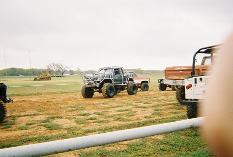 1989 Ford F-350 - Several heavily modified trucks are gathered on a dirt track under an overcast sky.