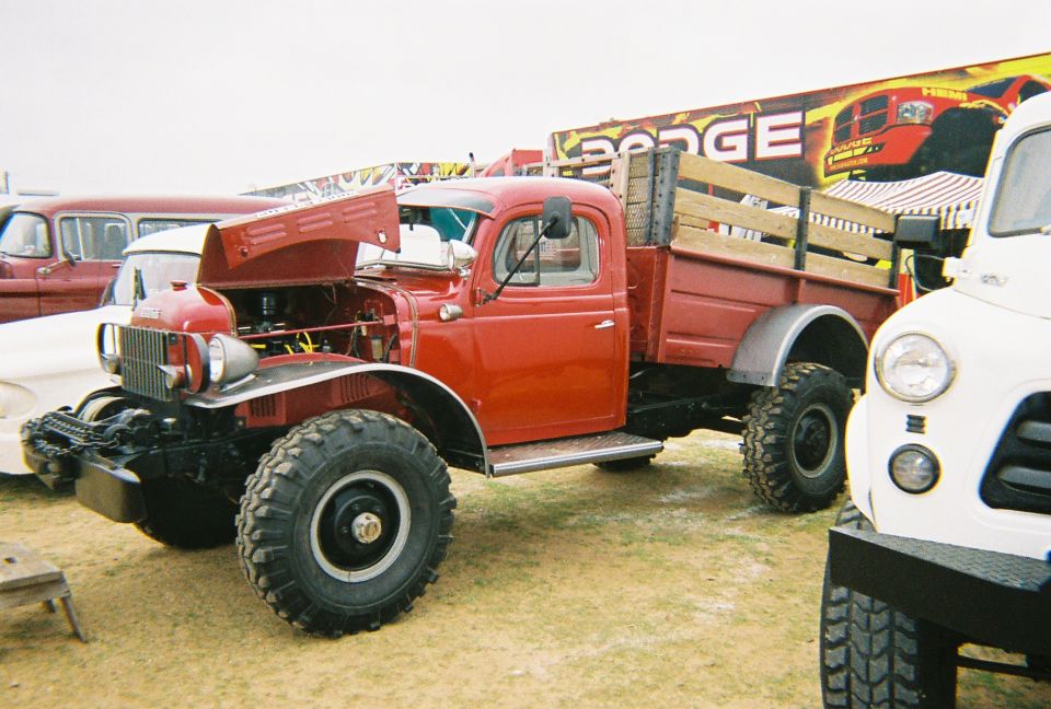 Red vintage Dodge Power Wagon with hood open, large off-road tires, wooden bed