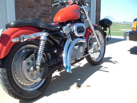 2002 Harley-Davidson Sportster Custom - A red 2002 Harley-Davidson Sportster Custom motorcycle is parked outside next to a brick building.