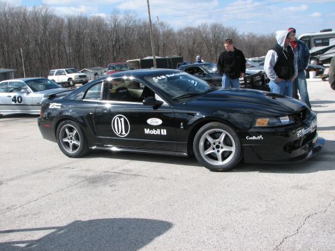 2000 Ford Crown Victoria - A black Ford Mustang Cobra is parked at a track, with other vehicles and people around.