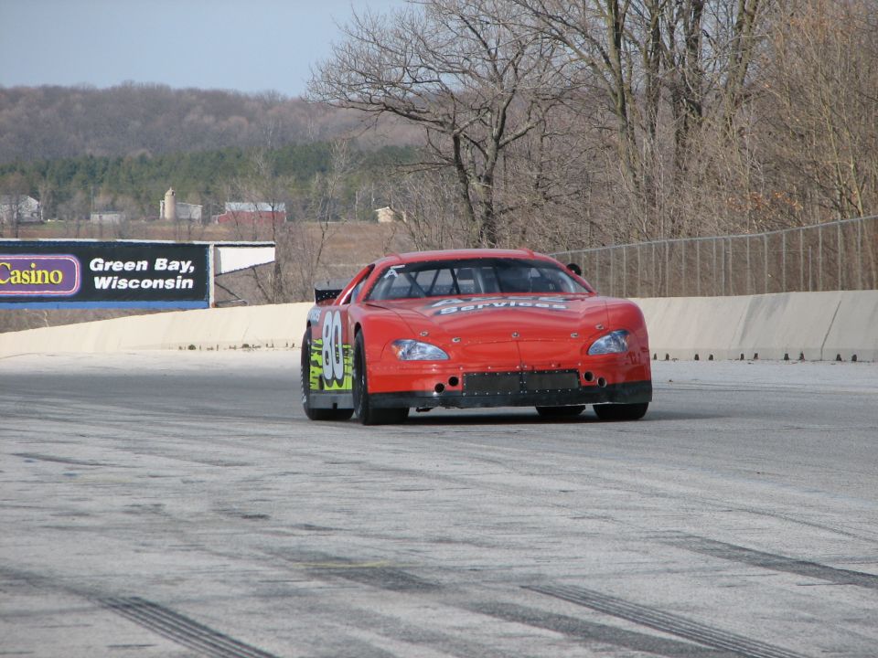 Red race car with number 80 on the side, on a track. Billboard in background says Green Bay, Wisconsin