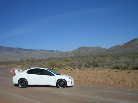 1996 Ford Probe - A white Dodge Neon SRT-4 is parked on a dirt road with a mountainous desert landscape under a clear blue sky.