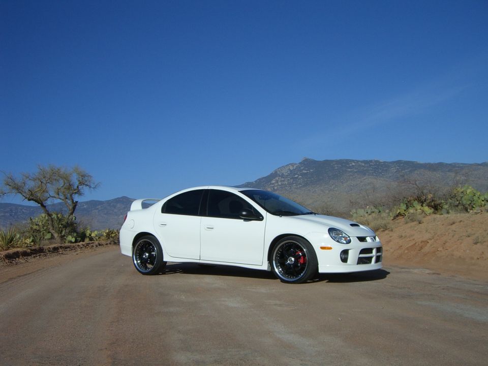 White sedan with black rims parked on a dirt road with mountains in the background
