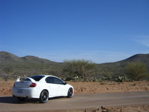 1996 Ford Probe - A white Dodge Neon SRT-4 is parked on a dirt road in a desert landscape under a clear blue sky.