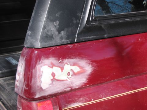 1991 Ford Bronco - Rear quarter panel of a red SUV showing damage and body filler work.