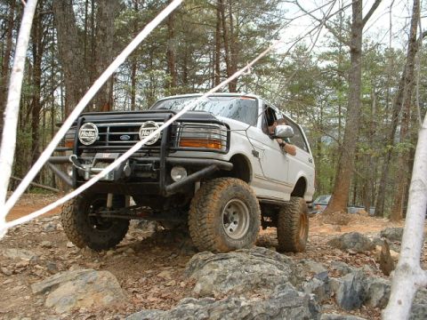 1987 Ford F-150 - Modified Ford Bronco tackling a challenging rocky trail in a wooded area.