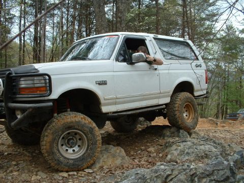 1987 Ford F-150 - A white Ford Bronco navigates a rocky off-road trail, with another vehicle visible in the background.
