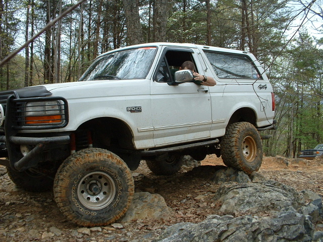 White Ford Bronco climbing over rocks on a trail. Driver is visible
