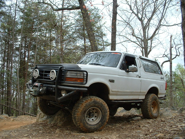 White Ford Bronco with off-road modifications, including a brush guard and winch, on a rocky trail