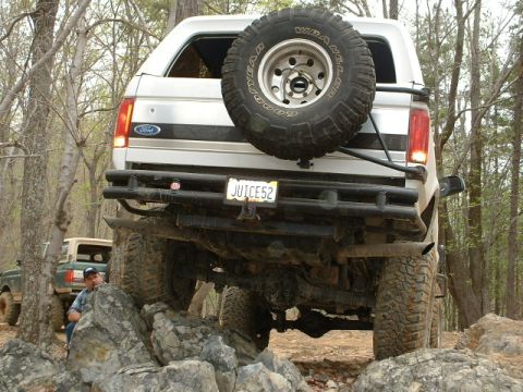 1987 Ford F-150 - A white Ford Bronco navigates a rocky trail, with another Bronco visible in the background.