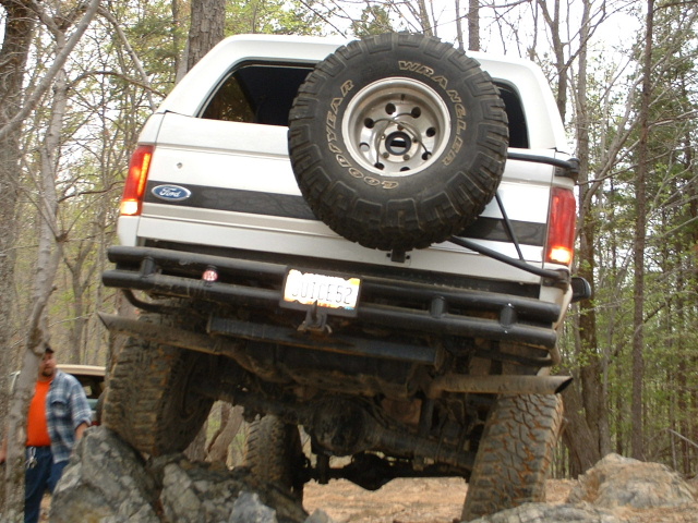 White 1987 Ford Bronco with spare tire on rear, off-roading over rocks