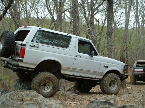 1987 Ford F-150 - A white Ford Bronco tackles a challenging off-road trail, with another vehicle visible in the background.